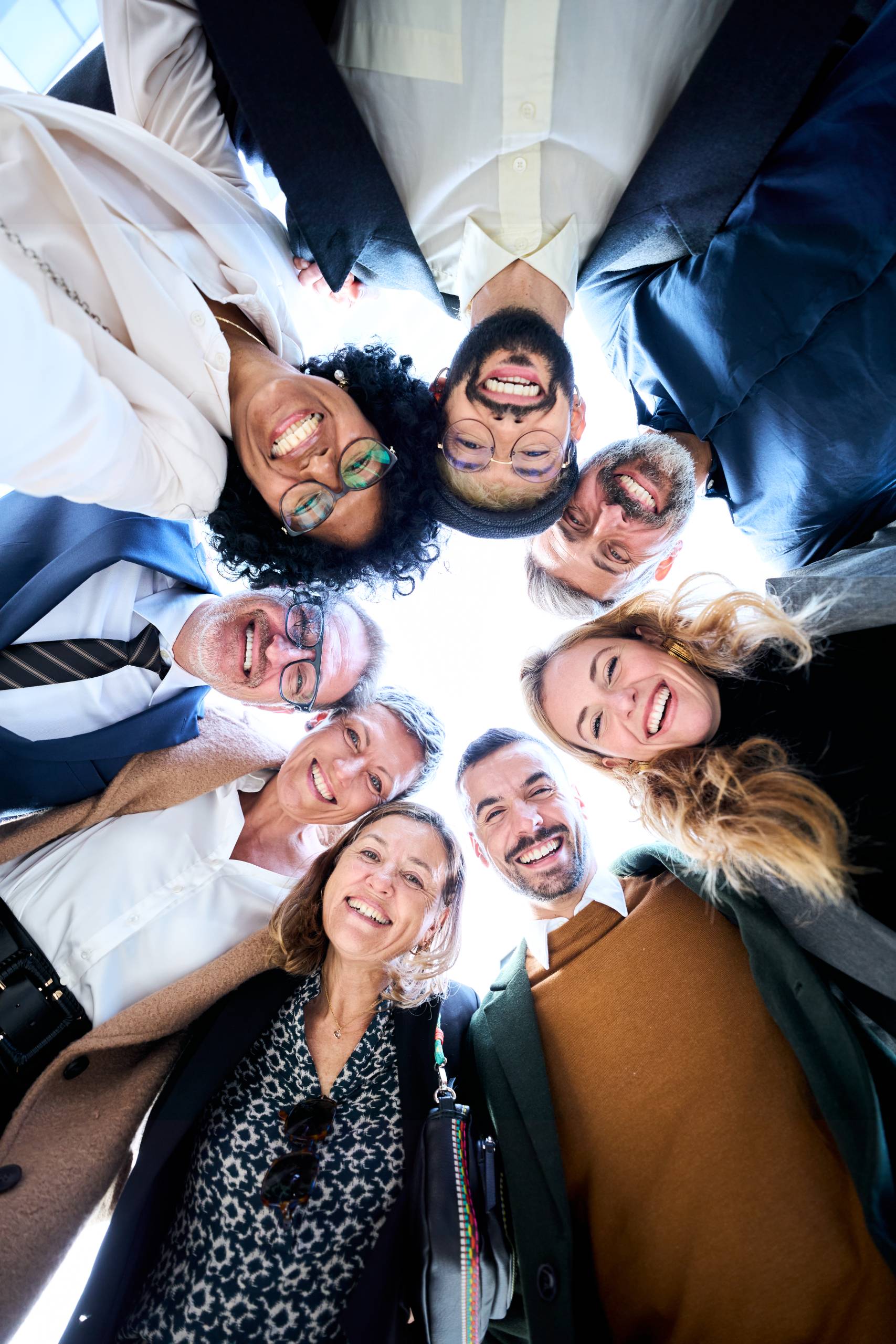 Vertical low angle view of cheerful group of diverse business people in formal wear are gathered in a circle, sharing smiles embracing together as a gesture of unity and celebration success