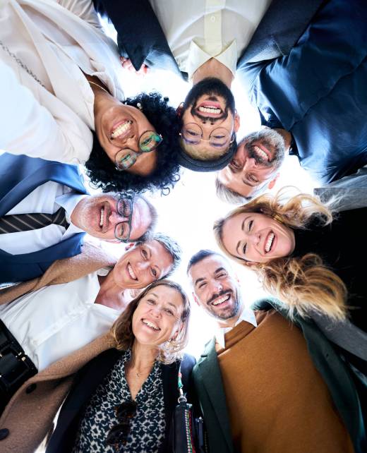 Vertical low angle view of cheerful group of diverse business people in formal wear are gathered in a circle, sharing smiles embracing together as a gesture of unity and celebration success